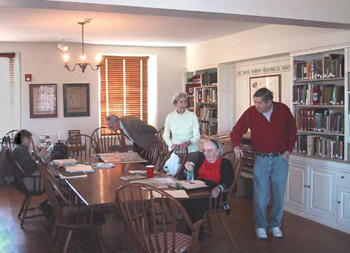 room with built-in bookshelves, two people seated at large table in center, two people standing
