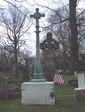 grave marked by a cross on a tall tapered column; veteran's flag marker on the side