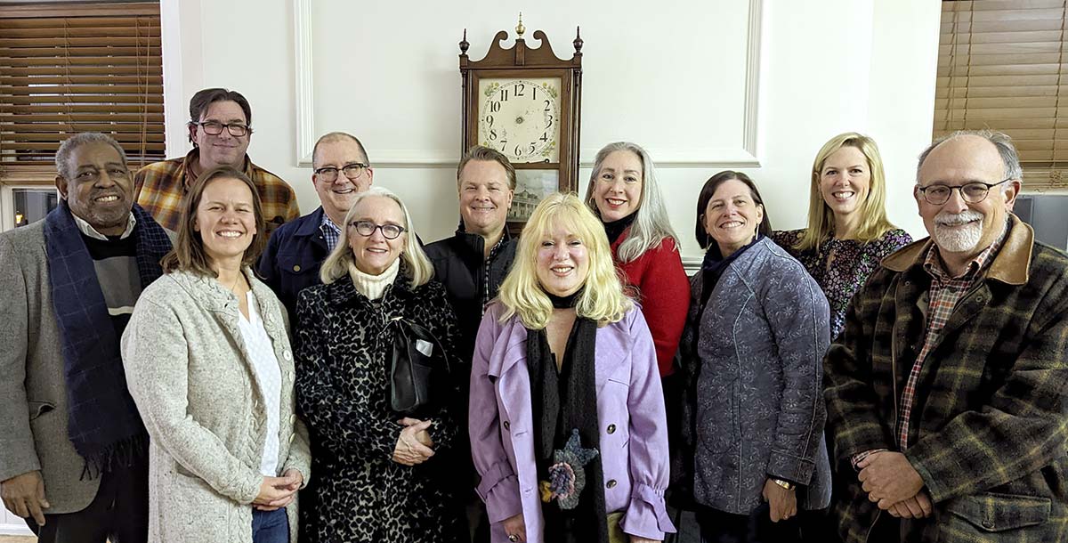 11 board members posed in front of a mantle with an antique clock at the Lower Merion Academy