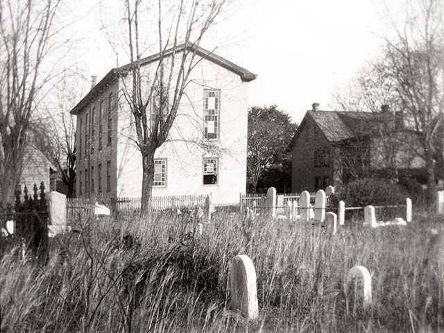 gravestones in long grass, rear of church in background