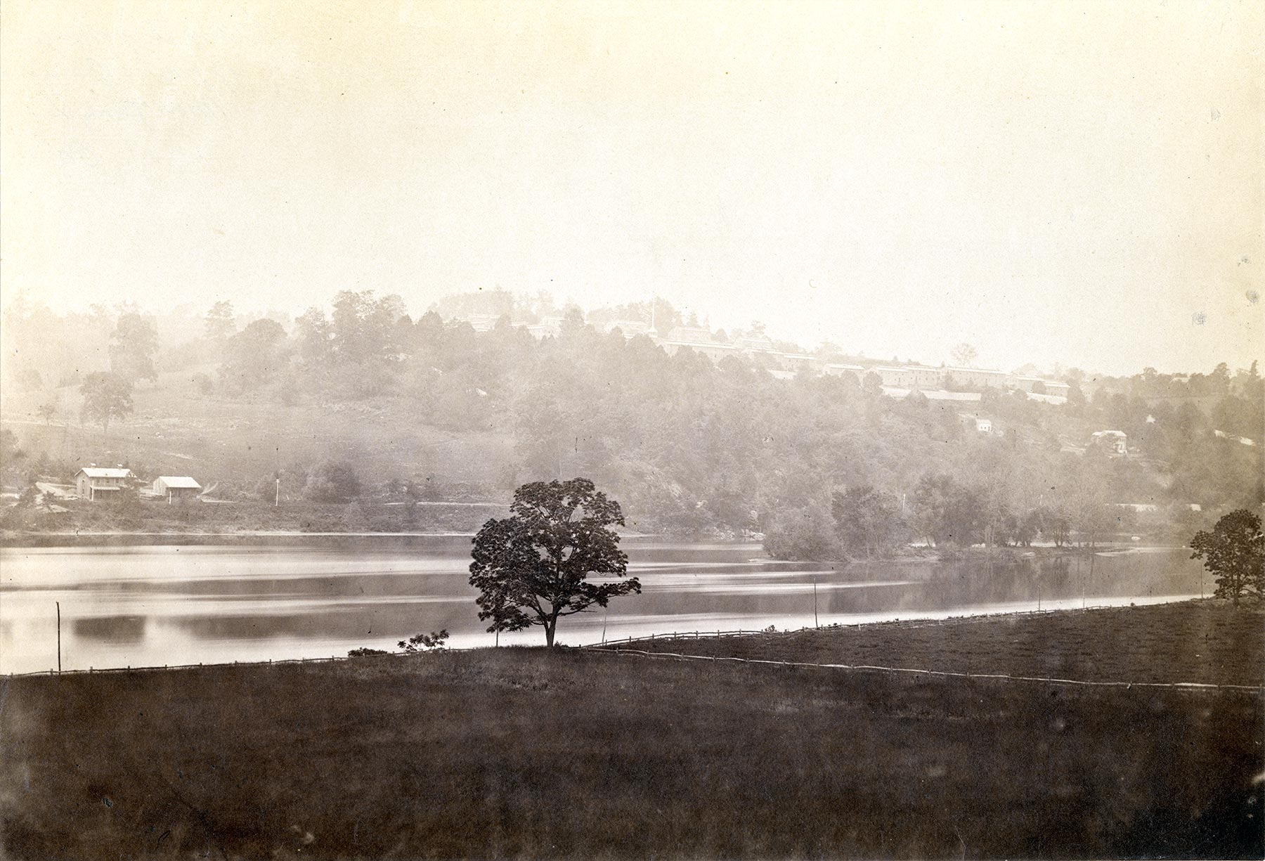 misty rural countryside looking across river to a wooded hill with buildings at crest