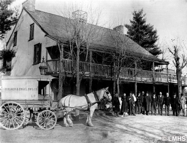 Horse pulling a delivery cart and row of men lined up in front of the inn