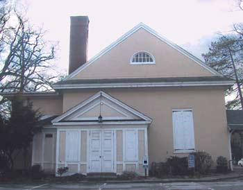 The front of the meeting house, a plain stuccoed building with white doors, shutters and a brick chimney