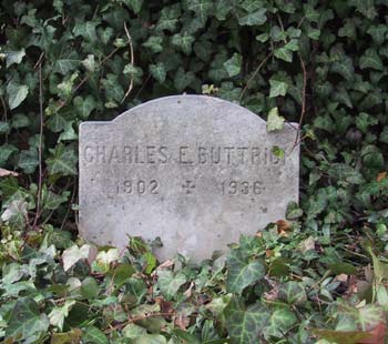 short, simple grave stone of Charles E. Buttrick surrounded by ivy