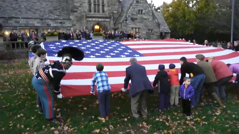 dozens of men, women and children fold a giant American flag at dusk