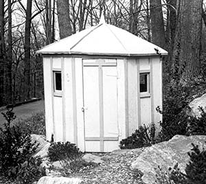 small oct/hexagonal white wood building with a door and 2 windows